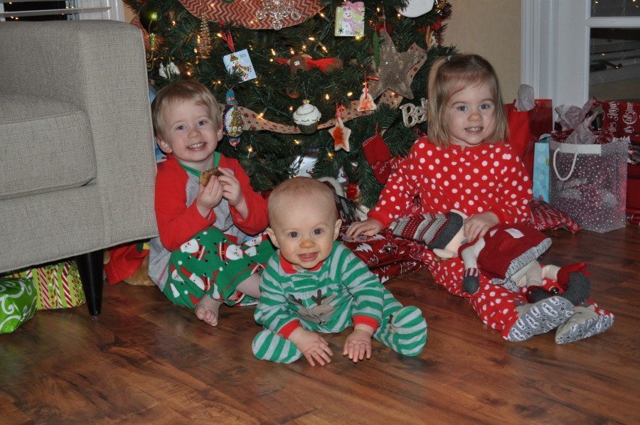 twin toddlers and a baby in pajamas under christmas tree third baby after twins