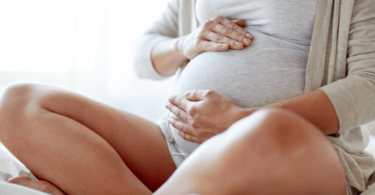 pregnant woman sitting cross legged on a bed and holding her belly