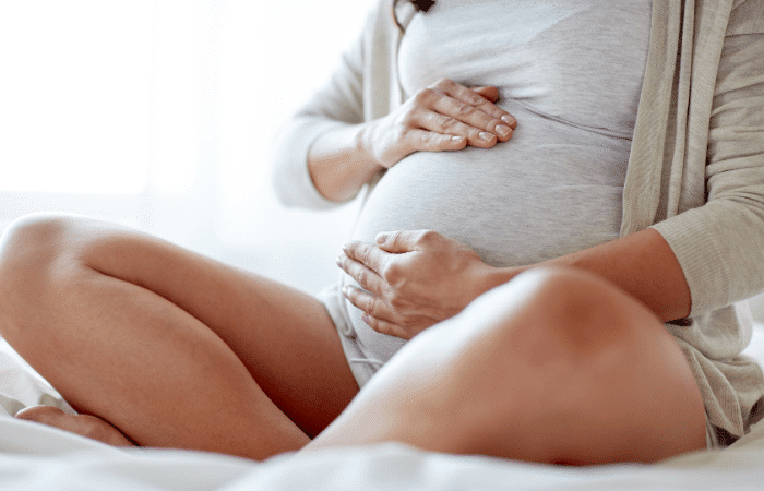 pregnant woman sitting cross legged on a bed and holding her belly