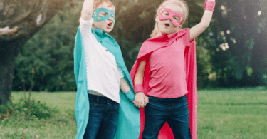 two children with superhero outfits and hands aimed at the sky