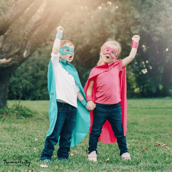two children with superhero outfits and hands aimed at the sky