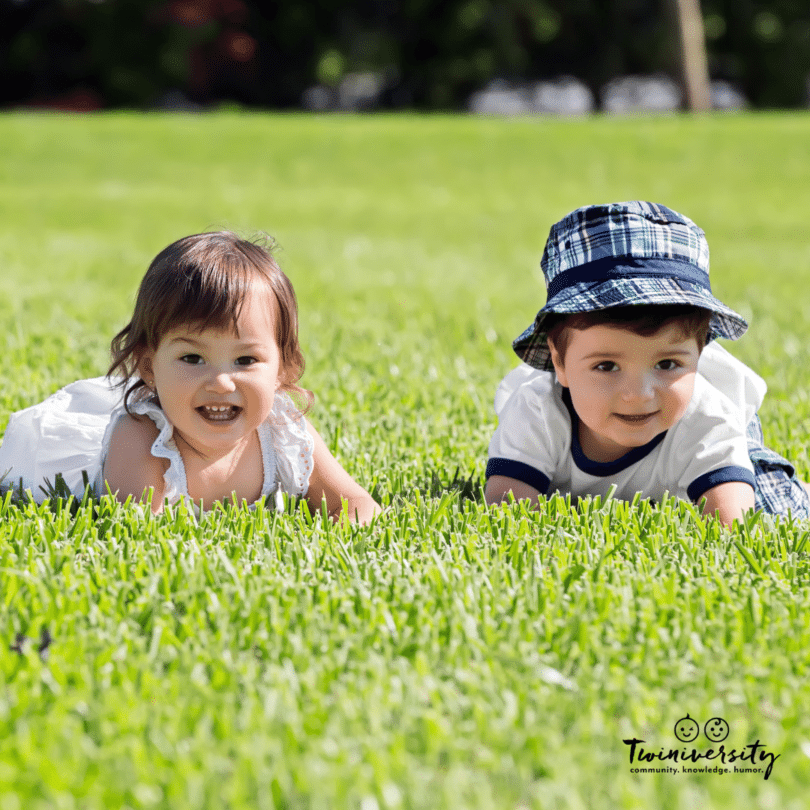 twin boy and girl toddlers laying on the grass outside