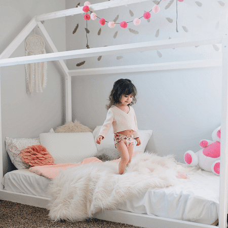 toddler bed for twins girl standing on white toddler bed smiling