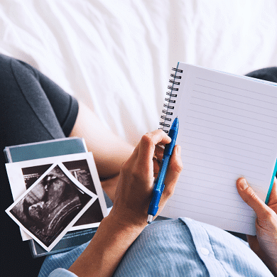 twins ultrasound pregnant woman holding ultrasound pictures on her lap and a notepad and pencil to take notes