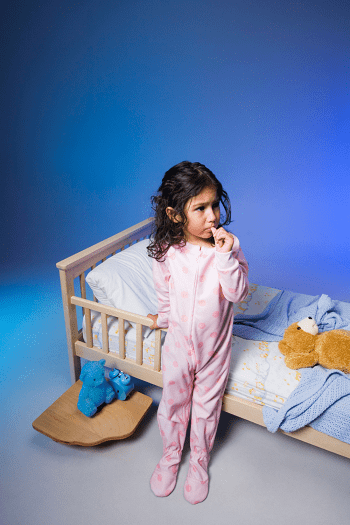 toddler bed for twins girl standing next to toddler bed with pink pajamas on