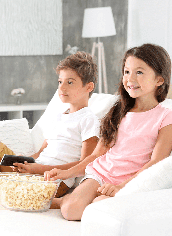 leftover Halloween candy 2 children watching tv with the boy holding the remote control and the girl reaching fro some popcorn