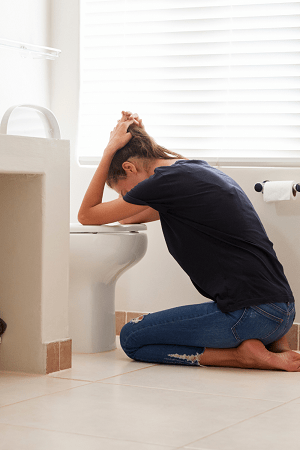 twin pregnancy symptoms woman kneeling over a toilet with her head in her hand, feeling nauseous