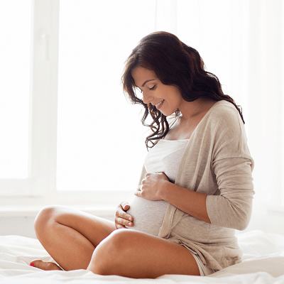 twin pregnancy symptoms woman sitting with her legs crossed while holding her pregnant belly, smiling