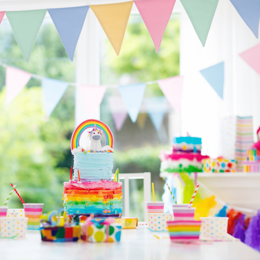 twins' birthday cake with a rainbow and unicorn on top, and cups with colored straws on a table