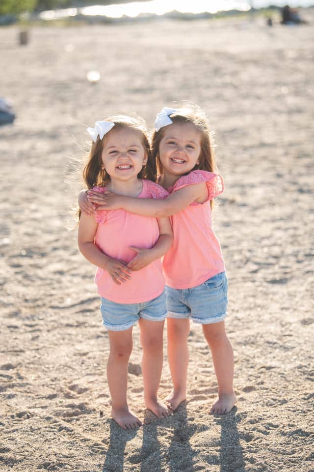 twin toddler girls hugging on the beach dressing twins alike