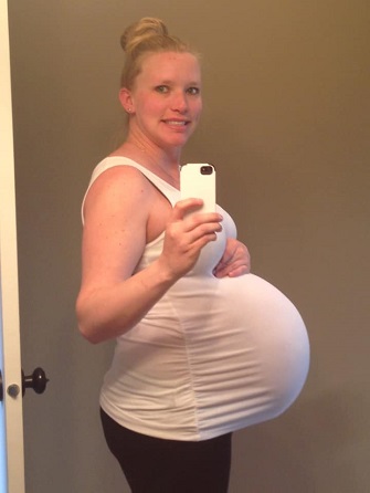 pregnant with twins belly woman holding pregnant belly while taking a mirror selfie with one hand
