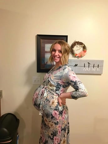 pregnant woman smiling and holding her back while showing off belly in floral dress