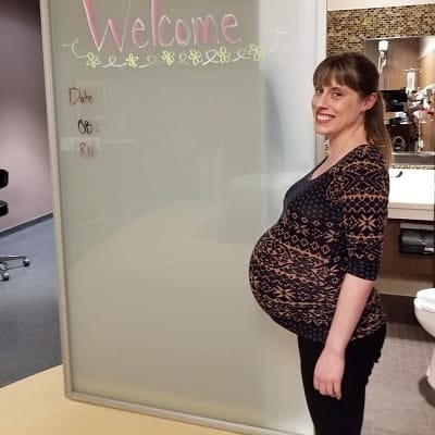 pregnant with twins belly pregnant woman smiling while standing in front of a hospital welcome to OB sign