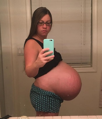 pregnant with twins belly. A pregnant woman holding her phone for a picture showing off very pregnant belly