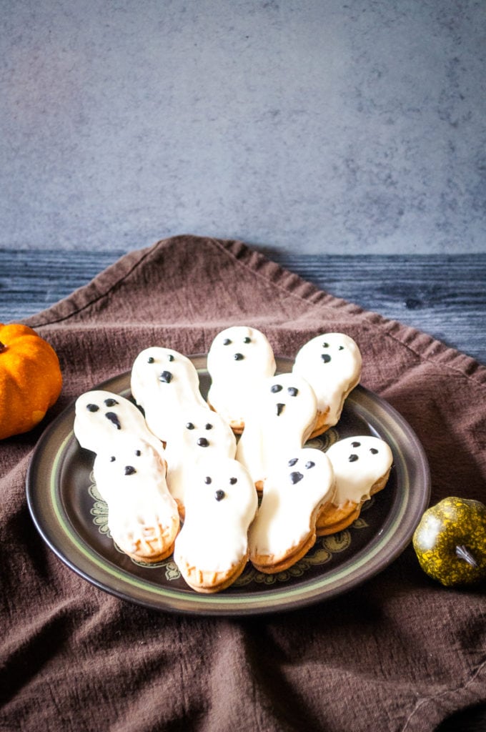 ghost cookies nutter butters on a plate dripping with white chocolate and eyes and a nose drawn on