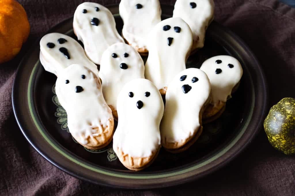 ghost cookies nutter butters on a plate dripping with white chocolate and eyes and a nose drawn on