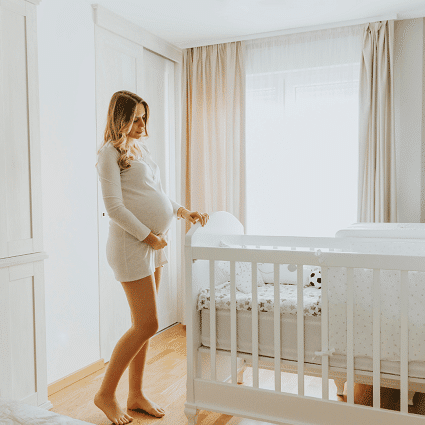 crib mattress dimensions. pregnant woman looking at put together crib while holding belly