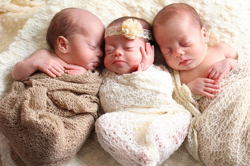 having triplets 3 infants, 2 boys and 1 girl, wrapped in blankets and laying on a large blanket together