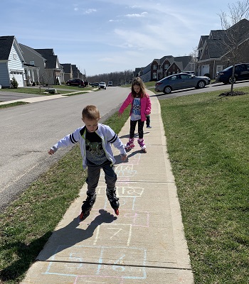 physical activities a boy and girl on rollerblades on a sidewalk with a hopscotch board drawn on it in chalk