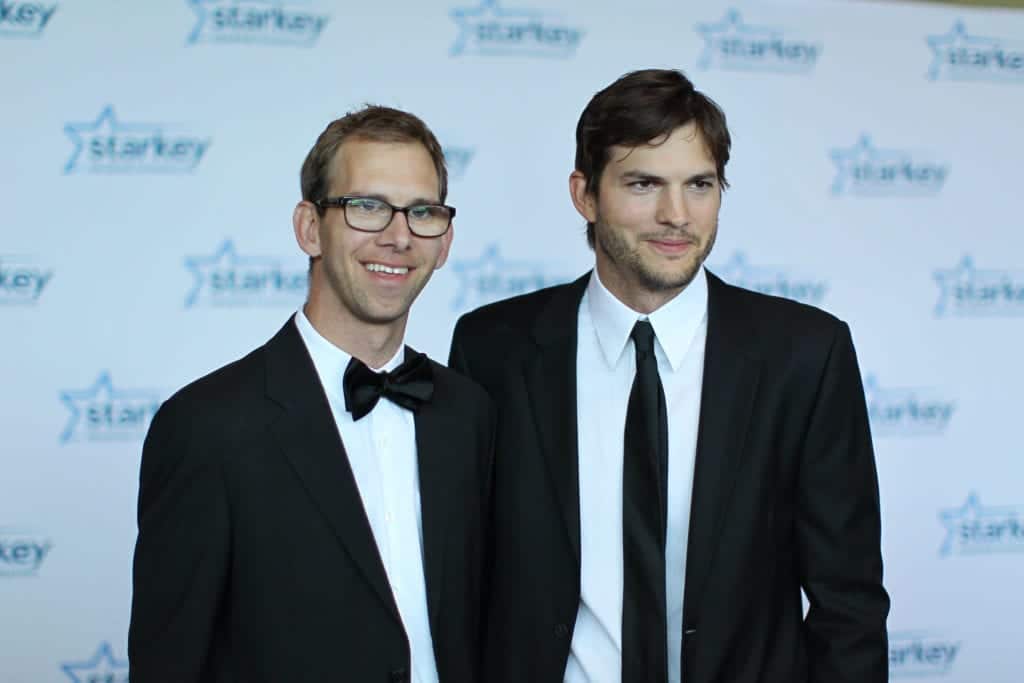 Celebrity twins two men in tuxedos on a red carpet posing for a picture while smiling. 