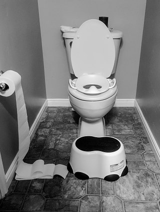 potty training regression black and white toilet with potty seat on top and a stool in front of it