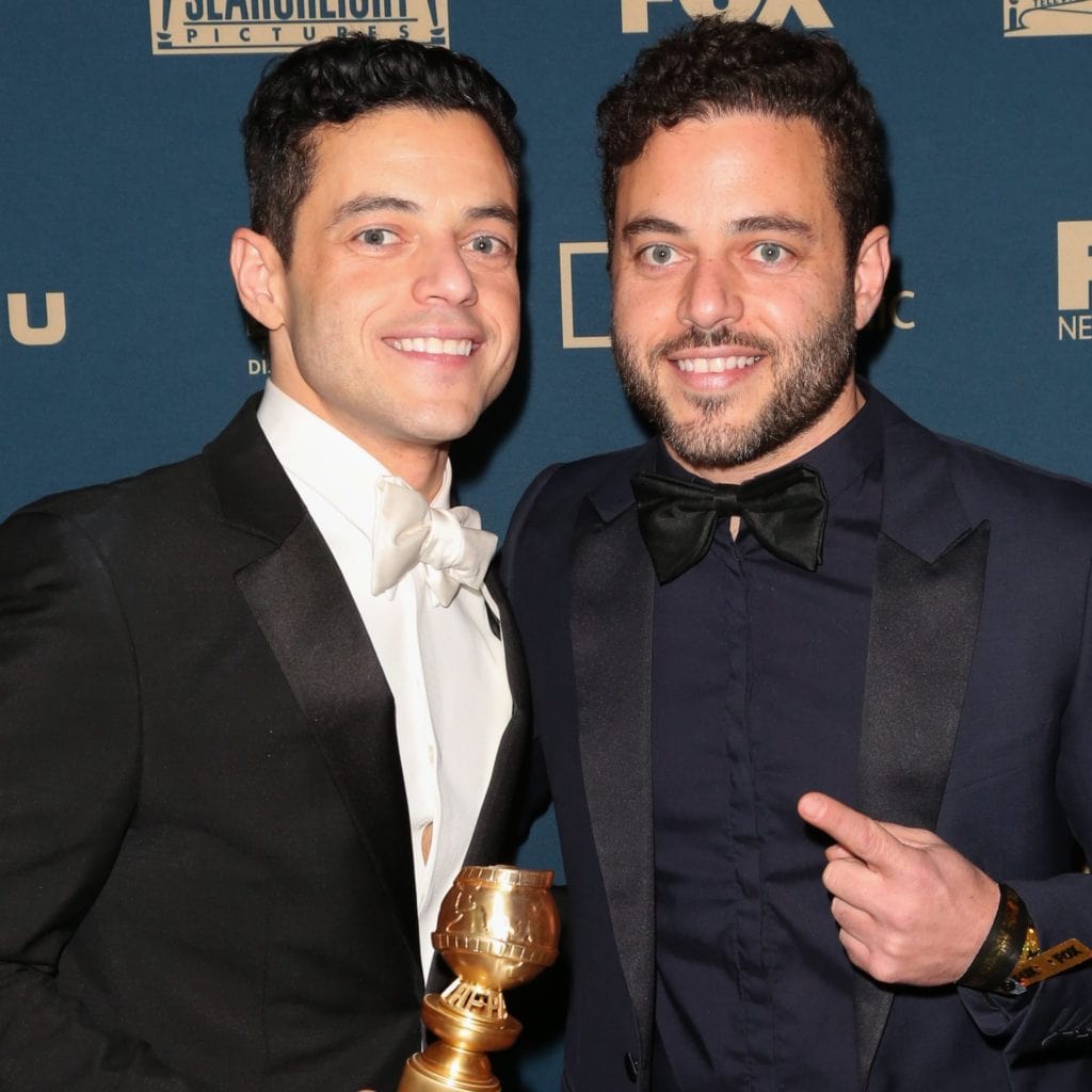 Celebrity twins identical twins in tuxedos smiling, 1 holding an award.