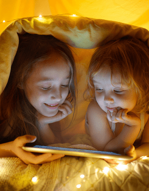 two little girls watching a tablet under a blanket