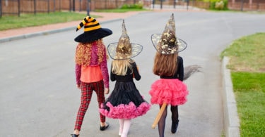 trick or treating COVID three girls wearing halloween costumes walking away down the street