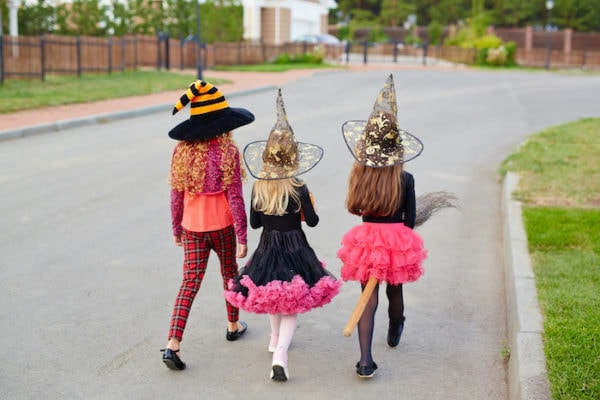 trick or treating COVID three girls wearing halloween costumes walking away down the street
