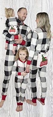 matching Christmas pajamas a man holding a baby and a woman holding hand with a little girl, all 4 in matching pajamas