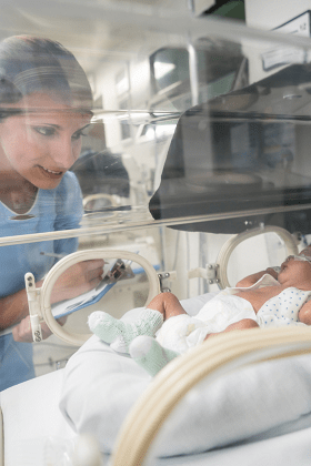 nicu nurse observe and taking notes on a baby in an enclosed isolette