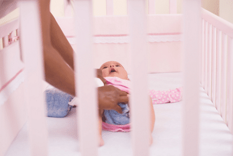 best crib sheets persons arms reaching into a crib to change a baby