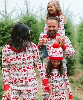 matching christmas pajamas a man with a toddler on his shoulders, a young girl and woman holing hand walking in a christmas tree farm