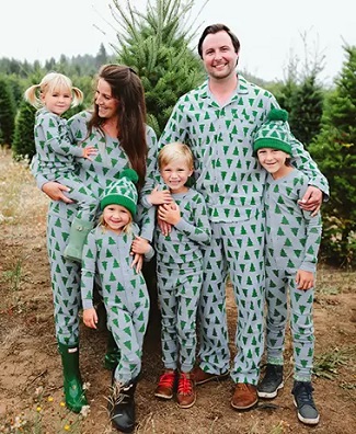 matching christmas pajamas a man and woman smiling with 4 young children, standing in front of a pine tree outside wearing matching pjs