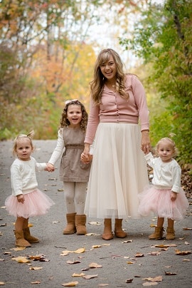 needy twins a woman and 3 little girls holding hands outside in the fall weather with leaves around on the ground