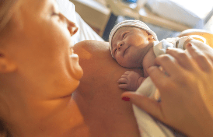 neonatologist woman holding a newborn baby on her chest and smiling as the baby looks up at her.