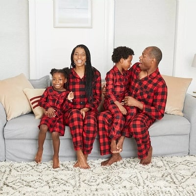 matching christmas pajamas a man with a boy on his lap laughing and a woman with her arm around a girl, all wearing matching pjs, sitting on a couch.