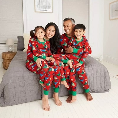 matching christmas pajamas a man with a woman sitting on a bed, each with a small child on their laps, all wearing matchings pjs