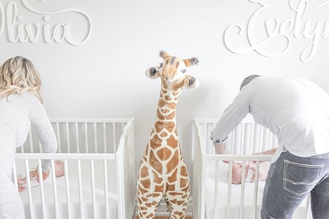 needy twins mom and dad changing diapers in cribs