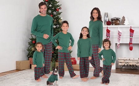 matching christmas pajams a man and woman with 4 children and a dog standing in front of a tree and fireplace with stocking, all dressed in matching pajamas