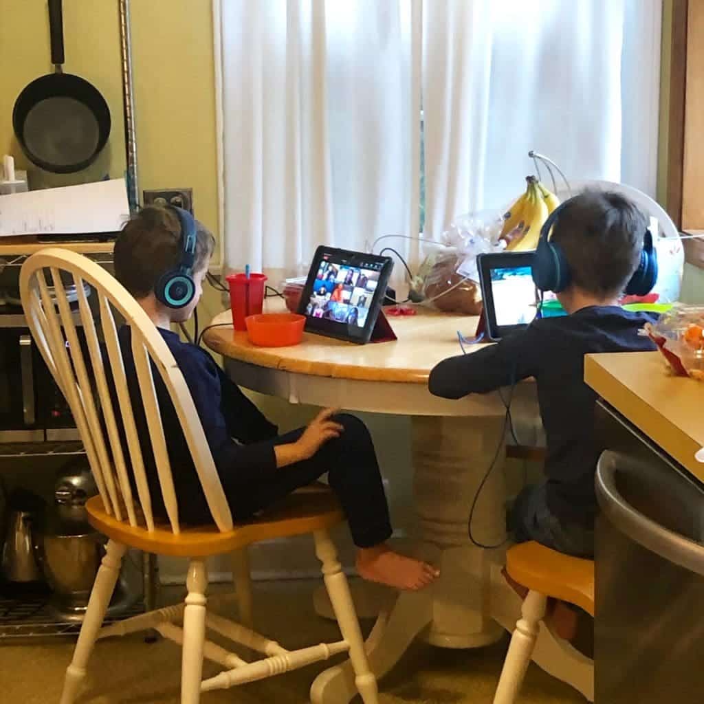 two boys sitting at a kitchen table with iPads and headphones on stress during covid