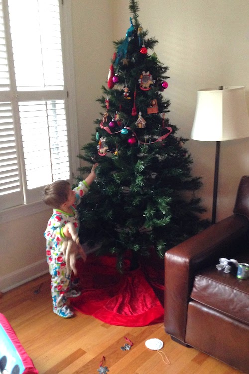 holiday safety tips child standing in front of a Christmas tree with no ornaments on the bottom