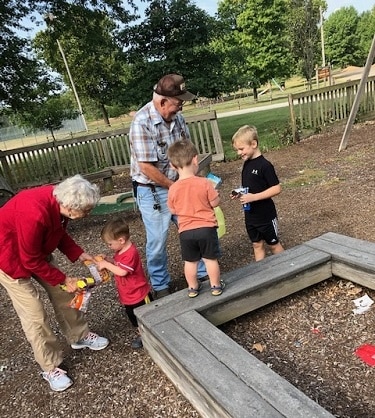 naughty list a grandma and grandpa handing out toys to 3 young children outside at a park