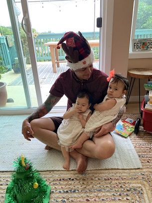 Christmas when you're broke a man with a holiday hat holding twins in his lap on the floor