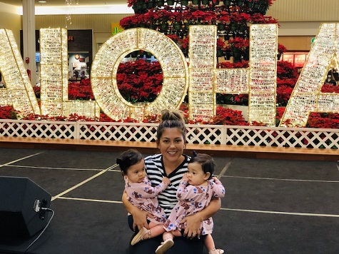 Christmas when you're broke a woman holding twin girls in front of a festively decorated "aloha" sign.