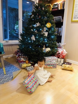 Christmas when you're broke. a little girl sitting on a floor in front of a Christmas tree, unwrapping a present