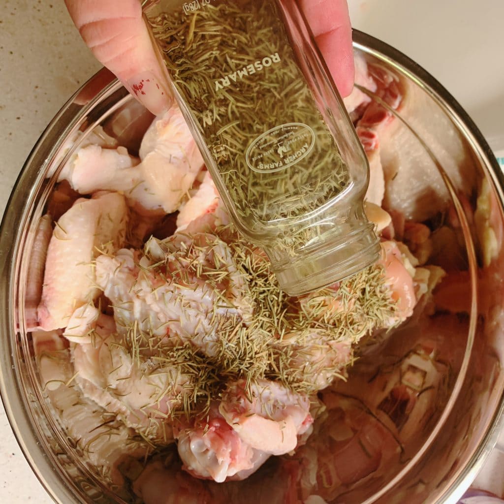 a hand sprinkling rosemary on raw chicken wings