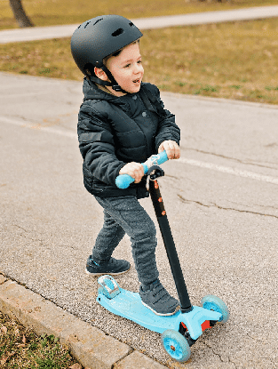 toddler scooter A boy in a helmet riding a scooter outside