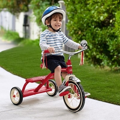 A boy on the sidewalk wearing a helmet riding a toddler tricycle