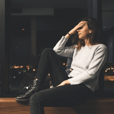 birth trauma a woman sitting on a windowsill, crying and holding her forehead.